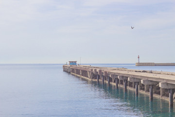 Fototapeta na wymiar Wooden boardwalk, calm sea and lighthouse in the background.