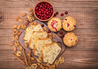 Homemade nut cake and cranberry muffins on wooden background.