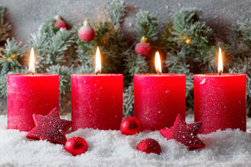 vier weihnachtlich geschmückte Kerzen im Schnee