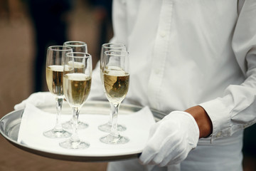 Waiter in white clothes holds tray with champagne flutes