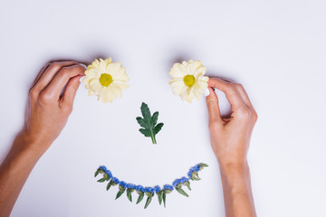 Women's hands make smiley from flowers on a white table