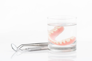 close up of dentures in glass of water and dental tool with noti