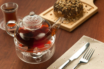 Transparent glass teapot and cup with tea on lerevyannoy surface brown and cookies on the board
