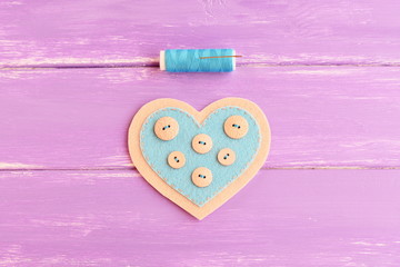 How to sew a felt heart decor. Step. Sew buttons with a blue thread on one side of a felt heart. Blue thread, needle on wooden background. Handmade souvenir for Valentine's day, wedding, mother's day