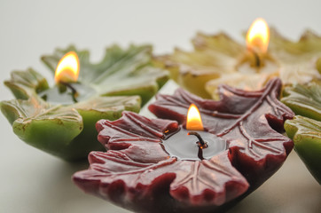 burning candles in the form of a leaf on a light background

