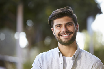 Smiling bearded young man sitting outside, portrait