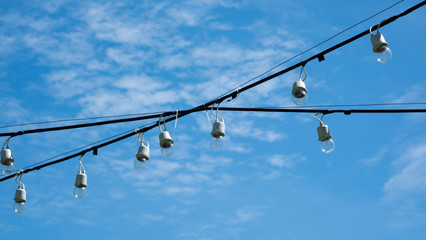Light bulbs on cross wire with cloudy sky in background