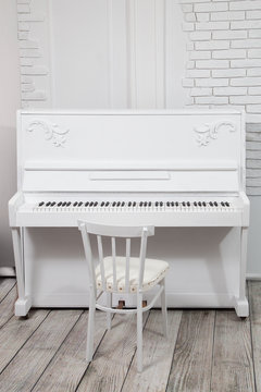 white piano with white stool in front of a white brick wall