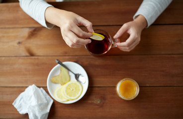 close up of woman adding lemon to tea cup