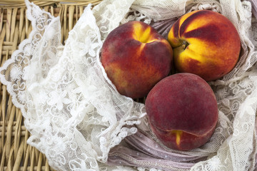 Three yellow and red peaches on the lacy shawl and wicker background