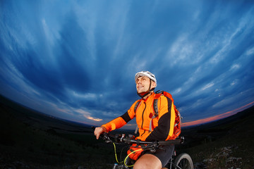 cyclist standing with mountain bike on trail at sunset