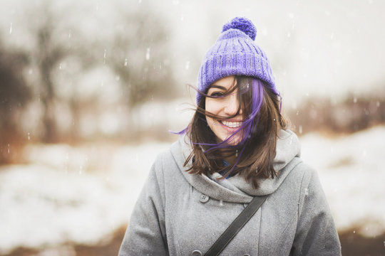 Cute happy young woman in beanie and coat outdoors in winter on windy day