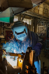 Worker with protective mask welding car part in automotive industrial