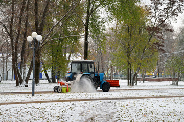 Snowplow cleans snow from the road in a Park on background of autumn trees. Horizontal orientation