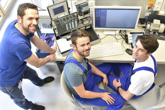 Portrait of smiling technical instructor with students at computer screen