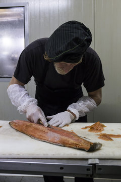 Fish smoker cleaning freshly smoked salmon with a knife
