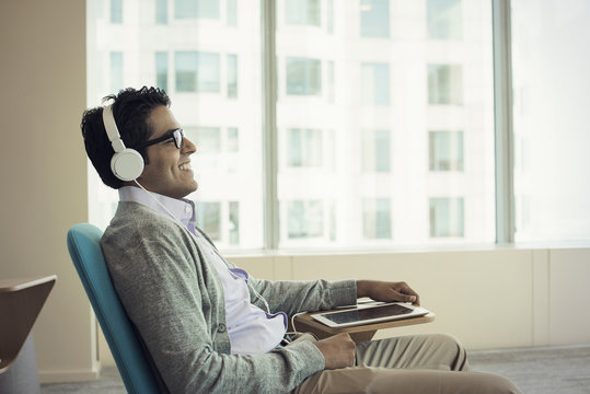 Businessman sitting in chair, wearing headphones, using digital tablet