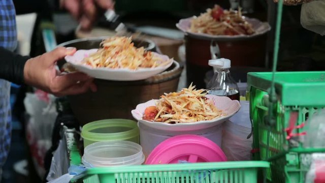 Female cook scooping SOMTUM, Green Papaya Salad, from mortar and putting into dishes and serving.
