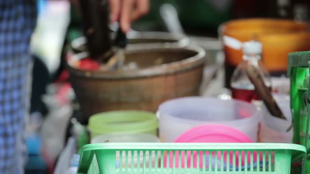 A female cook add papaya into mortar and pounding using pestel and scoop, gradually out of focus.
