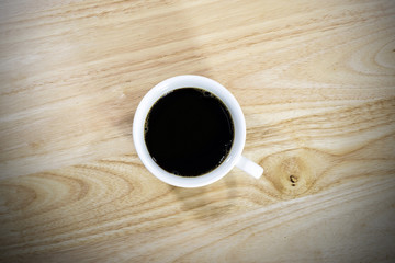 Top view of black coffee in a white ceramic coffee cup on the wooden floor.
