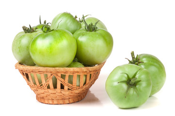 unripe green tomatoes in a wicker basket isolated on white background