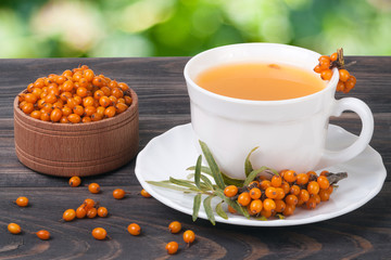Tea of sea-buckthorn berries on wooden table blurred garden background