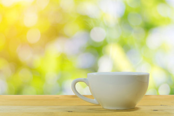 Close up of the white coffee mug on a wooden floor with a beautiful green nature background.