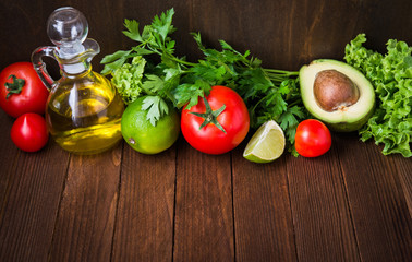 Fresh tomatoes, lime, avocado, lettuce, parsley and olive oil on dark wood background with space for text. Healthy food. Vegetables and greens. Salad ingredients.