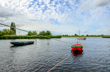 Red painted rowing boat moored to an iron pole in the water
