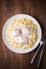 Pasta tagliatelle plate with meatballs and creamy sauce on dark wooden background top view. Italian cuisine. Delicious meal.