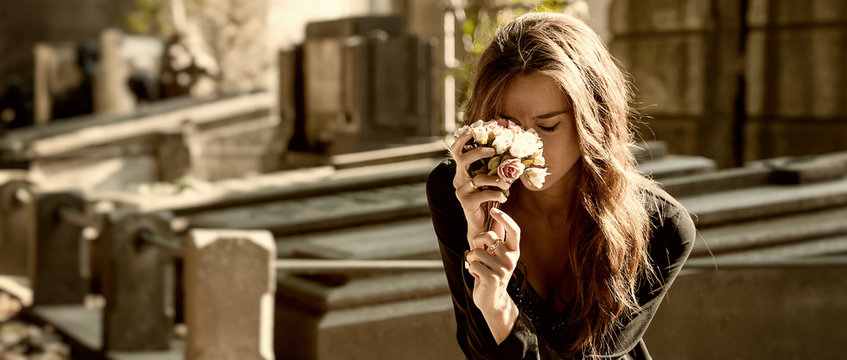 Sad woman holding bunch of flowers near a grave letterbox