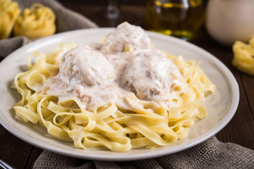 Pasta tagliatelle plate with meatballs and creamy sauce on dark wooden background close up. Italian cuisine. Delicious meal.