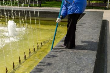 Woman in a blue coat is cleaning the fountain