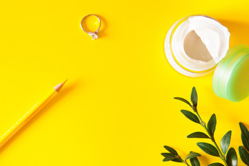 Pencil, ring, green leaves, face cream on bright yellow backgrou