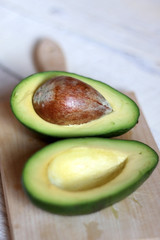 Avocado cut in half, on wooden board and rustic white table. Selective focus.