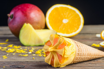 Ice cream cone with mango and orange on wooden table