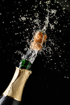 Champagne cork popping and splashing on black background