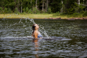 Fototapeta na wymiar Beautiful girl splashing her hear in an Swedish forest lake