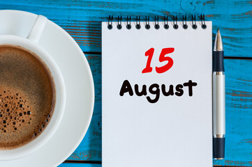August 15th. Day 15 of month, loose-leaf calendar on blue background with morning coffee cup. Summer time. Top view