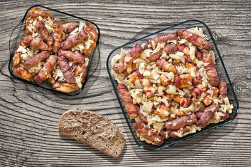 Grilled Minced Meat Loafs Cevapcici Rolled In Bacon With Chicken Thighs And Chopped Onion In Two Glass Baking Pans With Slice Of Bread Set On Old Knotted Cracked Wood