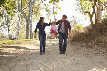 Obraz premium Couple walking on rural path lifting daughter, full length