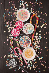 Colorful candies, lollypops and marshmallows on dark wooden background. Top view