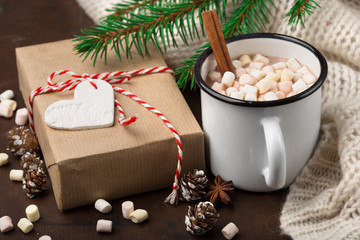 Cup with homemade Christmas hot Chocolate drink, Marshmallows and Holiday Gift on dark background. Winter time concept. Selective focus