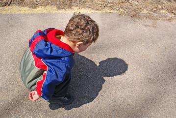 Toddler boy bending down examining his own shadow