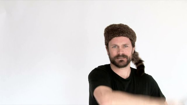 Model released man in studio wearing raccoon fur hat wielding a machete.
