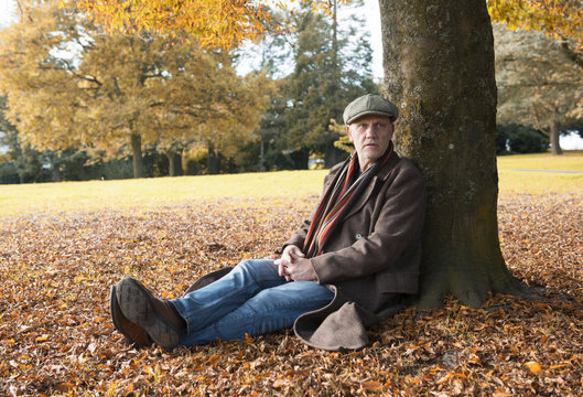 Portrait image of a happy mature man sitting under a tree in autumn 