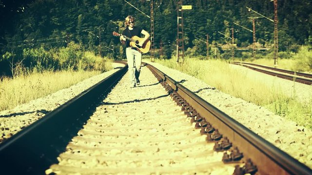 Very cool-looking left-handed long-haired guy walks along the railroad with his guitar