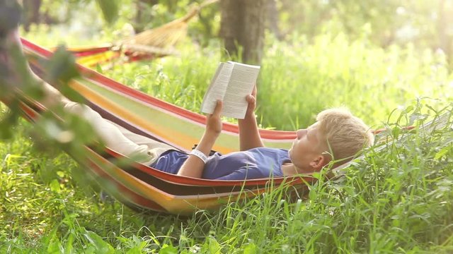Young man sways lying in the hammock and reads a book during siesta