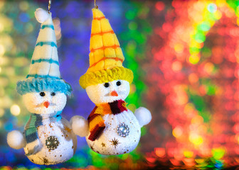 Two toy snowman on the background of colorful bokeh.