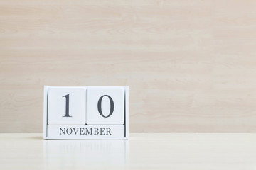 Closeup surface white wooden calendar with black 10 november word on blurred brown wood desk and wood wall textured background with copy space , selective focus at the calendar